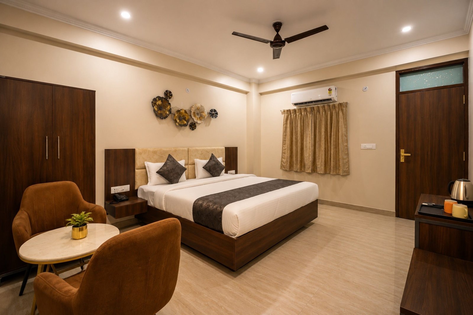 Guest room with a king bed, two tan armchairs by a round table and a brass wall display