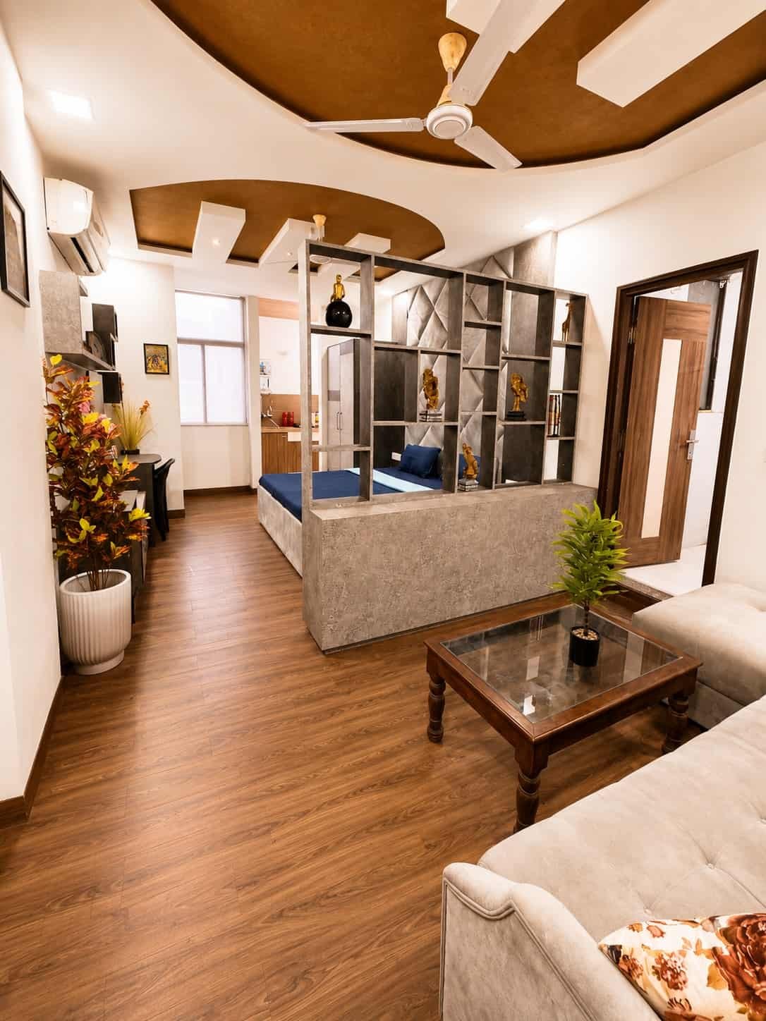 Studio with wooden floors, a sofa and coffee table, and an open shelf divider screening the bed