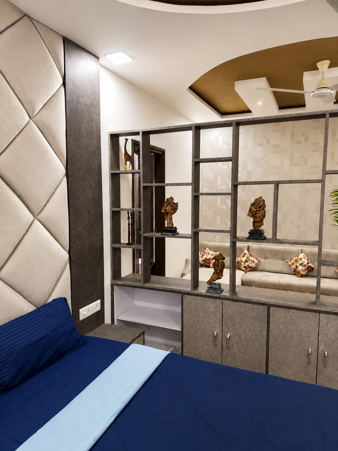 Bed with a navy cover in front of a padded wall panel and shelving