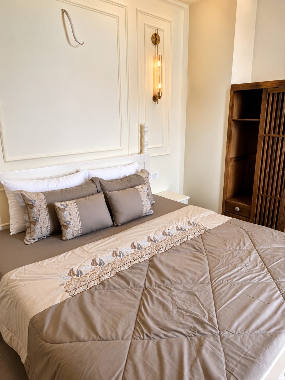 Bedroom 1 with a king bed in taupe linen and wall sconces on white panelled walls