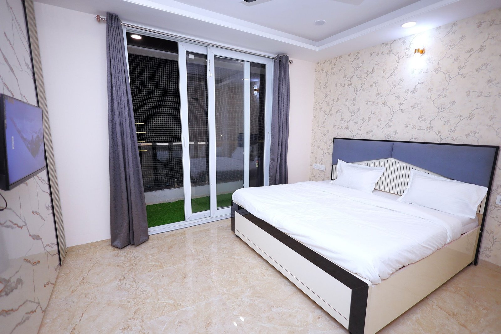 Bed with a grey headboard beside sliding glass doors to a balcony