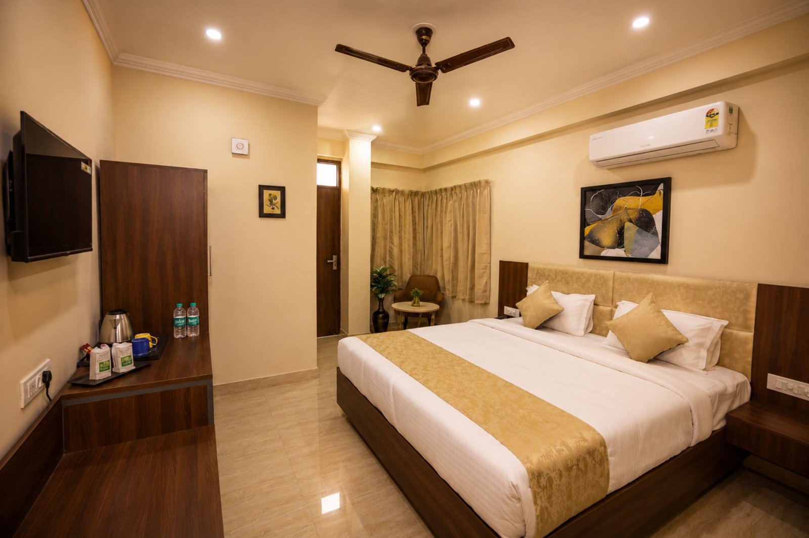 Guest room with a gold bed runner, a wall TV and a desk with a kettle