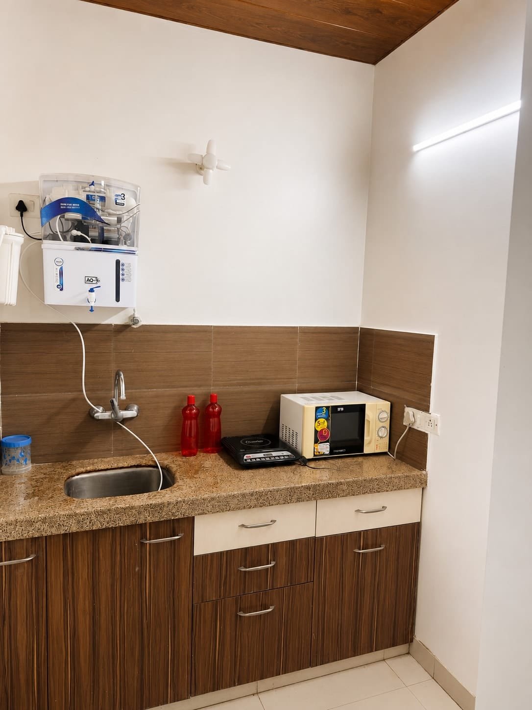 Kitchenette with wooden cabinets, sink, microwave and water purifier