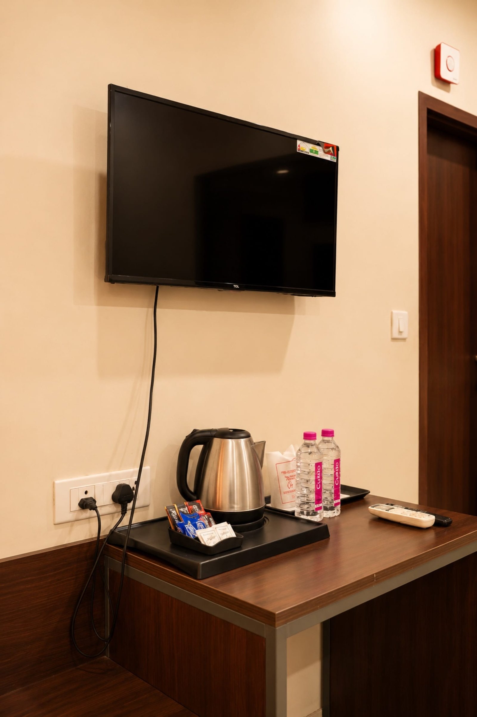 Wall TV above a desk with a kettle, tea tray and bottled water