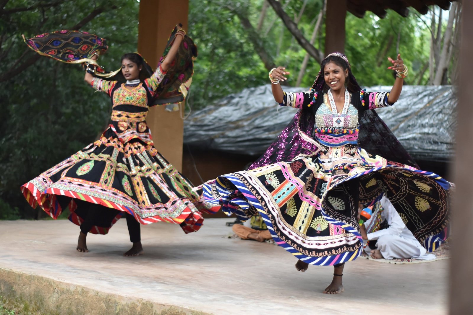 Two Kalbelia dancers mid-spin in black skirts embroidered with mirrors