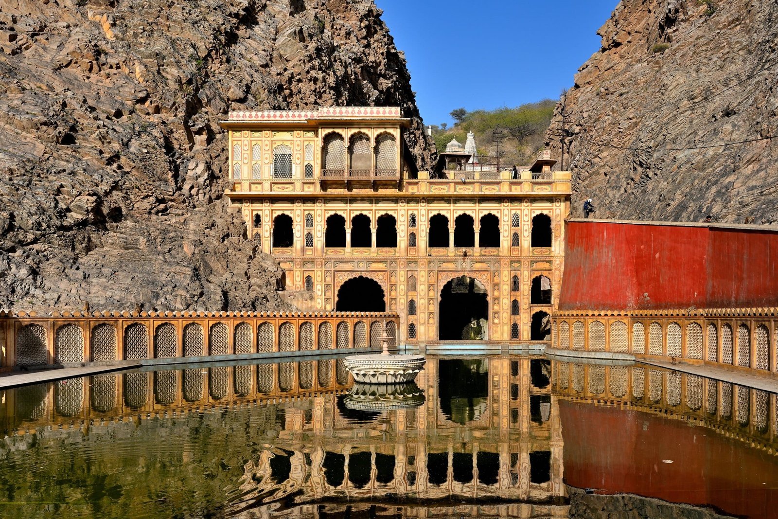 Galta Ji temple buildings reflected in a water tank below rocky hills