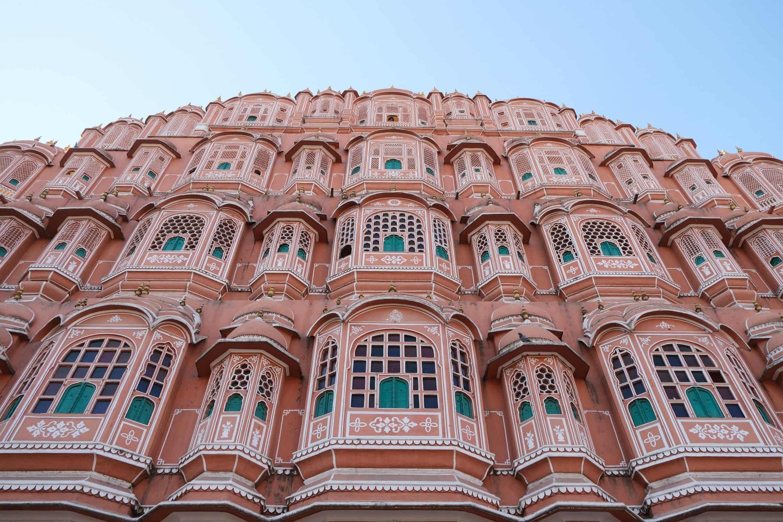 The pink sandstone face of Hawa Mahal, rows of small windows against a blue sky